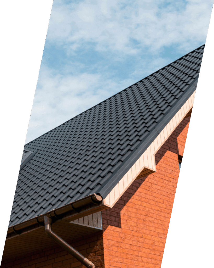 Steeply angled roof with black shingles on a red brick house against a blue sky.