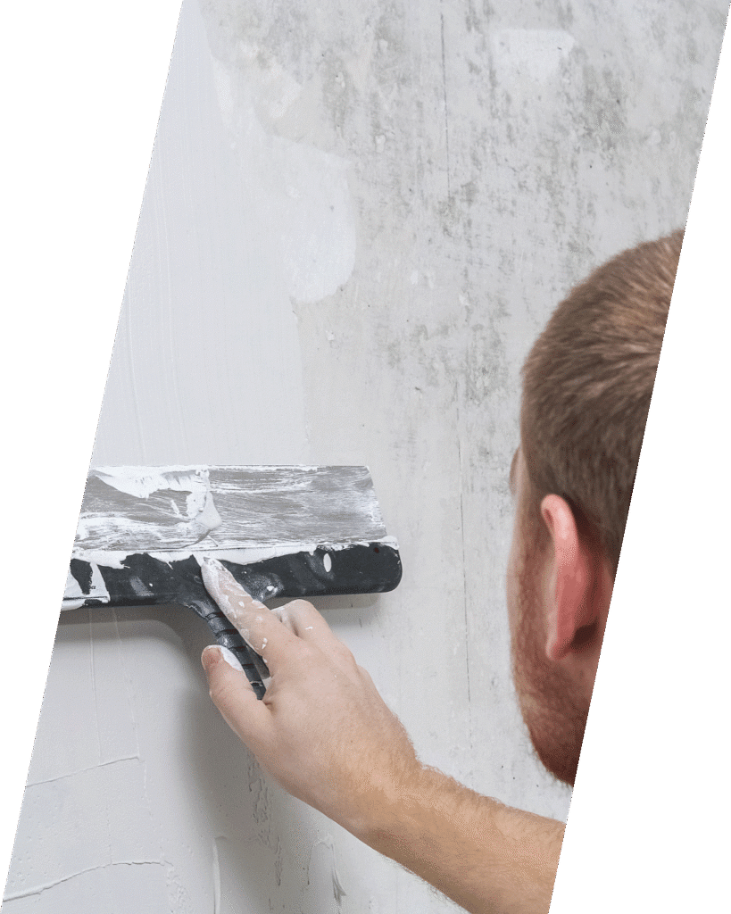 A person applies plaster to a wall with a trowel, smoothing the surface.