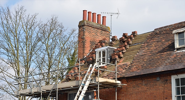 A brick house with scaffolding and a ladder leaning against it, undergoing roof repairs.
