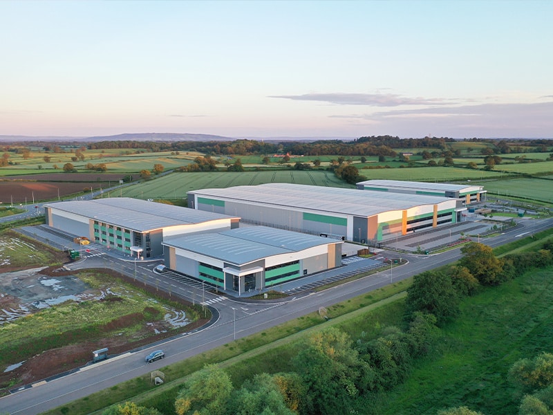 Aerial view of large industrial buildings with green accents set in a rural landscape.