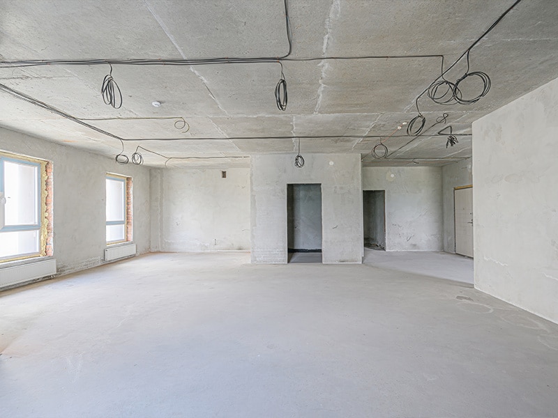 Spacious, unfinished room with concrete walls and ceiling, exposed wiring, and bare flooring.