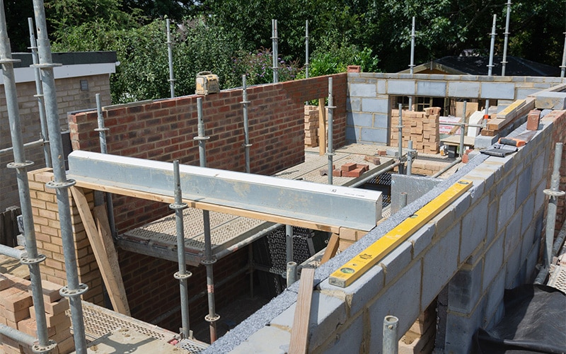 Construction site with partially built brick and cinder block walls, surrounded by scaffolding.